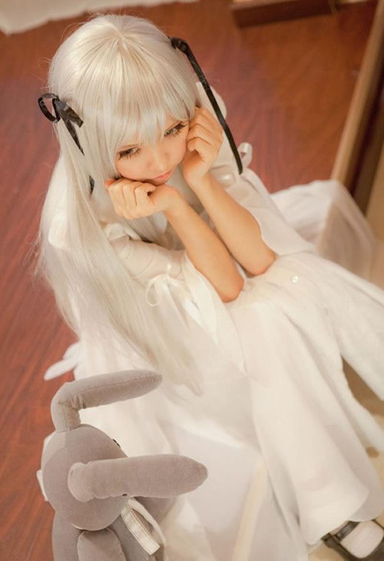 哀子扮演穹妹穿着白色连衣裙坐在室内木地板上，两手捧着脸