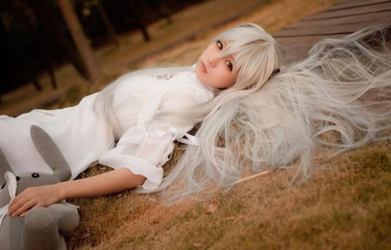 哀子扮演穹妹穿着白色连衣裙躺在枯黄的草地的木板上，手摸着兔子玩偶