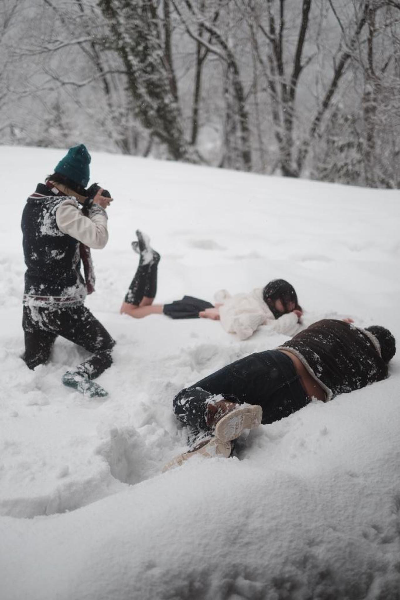 摄影们或跪或侧身躺在雪地，拍摄萌妹平地摔的照片